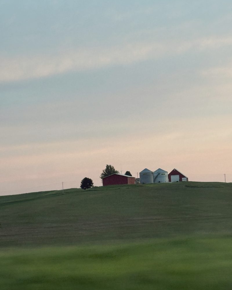 A red barn and grain bins on a green hill in western Iowa at dusk